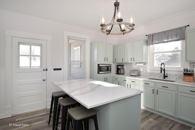 kitchen featuring stainless steel microwave, decorative light fixtures, tasteful backsplash, sink, and a center island