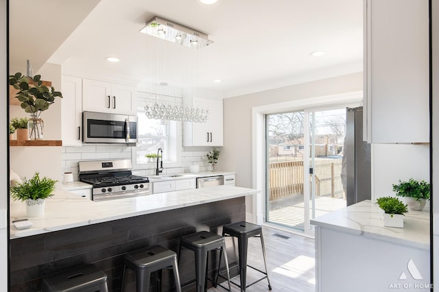 kitchen with sink, stainless steel appliances, light stone counters, white cabinets, and a kitchen bar