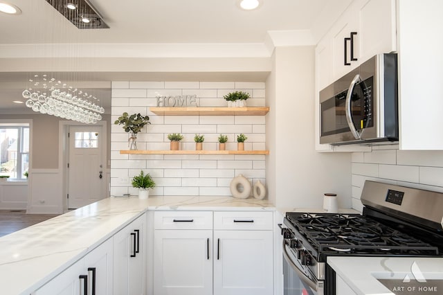 kitchen featuring light stone counters, crown molding, white cabinets, stainless steel appliances, and backsplash