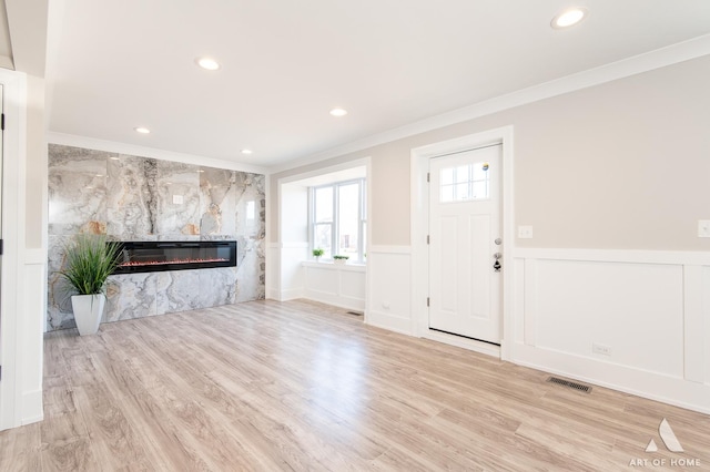 entryway featuring a premium fireplace, ornamental molding, and light hardwood / wood-style flooring