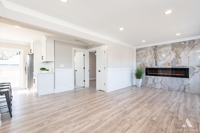 unfurnished living room with a fireplace, ornamental molding, and light wood-type flooring