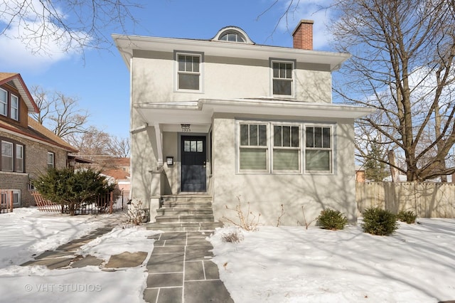 american foursquare style home featuring entry steps, a chimney, fence, and stucco siding