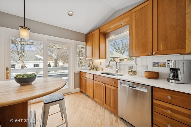 kitchen with pendant lighting, lofted ceiling, light countertops, stainless steel dishwasher, and a sink