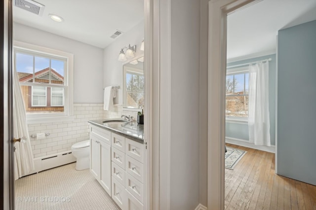 bathroom with tile walls, a wealth of natural light, visible vents, baseboard heating, and vanity