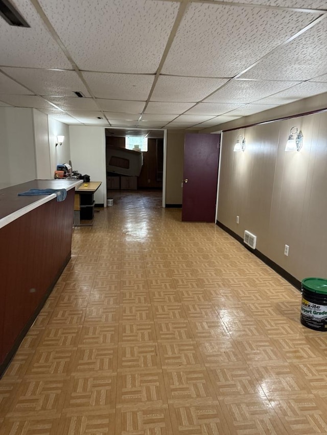 basement featuring light parquet floors, a paneled ceiling, and wood walls