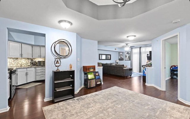 interior space featuring dark wood-type flooring, a ceiling fan, baseboards, stainless steel gas stove, and tasteful backsplash