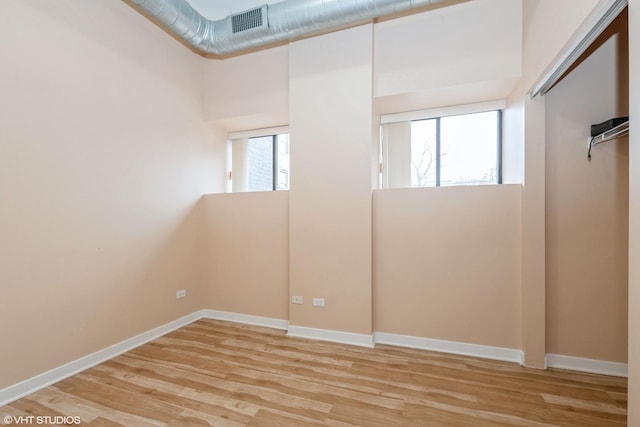 unfurnished room featuring light wood finished floors, plenty of natural light, visible vents, and baseboards