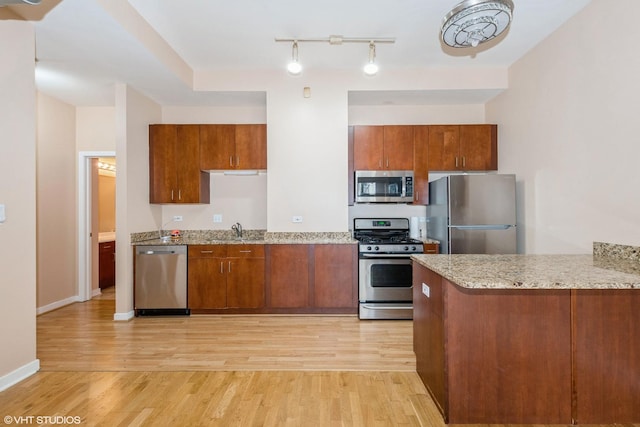 kitchen with light wood-style flooring, appliances with stainless steel finishes, a peninsula, light stone countertops, and a sink