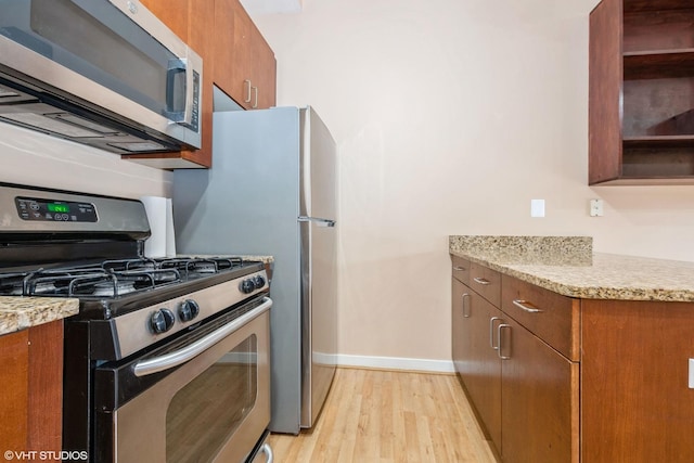 kitchen featuring brown cabinets, open shelves, stainless steel appliances, light wood-style floors, and light stone countertops