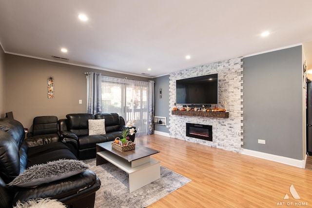 living room with hardwood / wood-style flooring, ornamental molding, and a stone fireplace