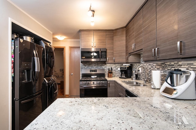 kitchen with stacked washer and dryer, sink, light stone counters, appliances with stainless steel finishes, and decorative backsplash