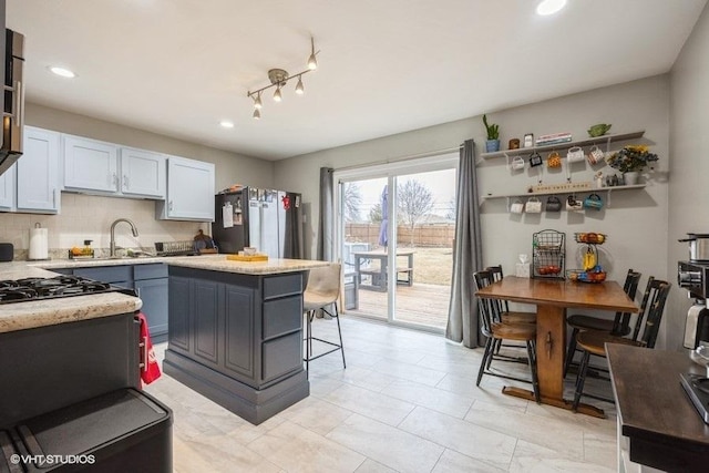 kitchen with sink, a breakfast bar area, tasteful backsplash, stainless steel fridge, and white cabinets