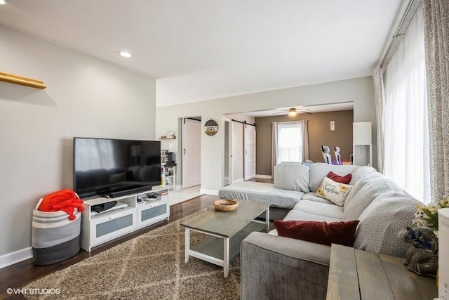 living room featuring dark wood-type flooring, ceiling fan, and a barn door