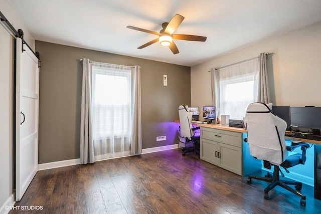 home office featuring dark wood-type flooring, plenty of natural light, a barn door, and ceiling fan