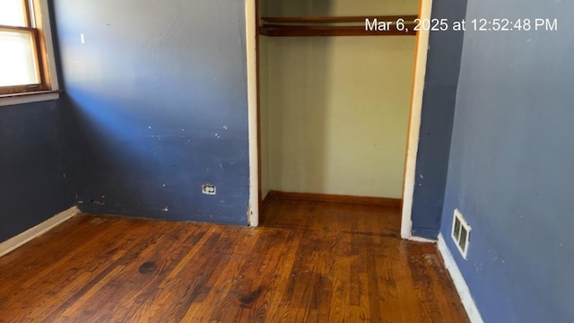 unfurnished bedroom with a closet, visible vents, baseboards, and wood finished floors