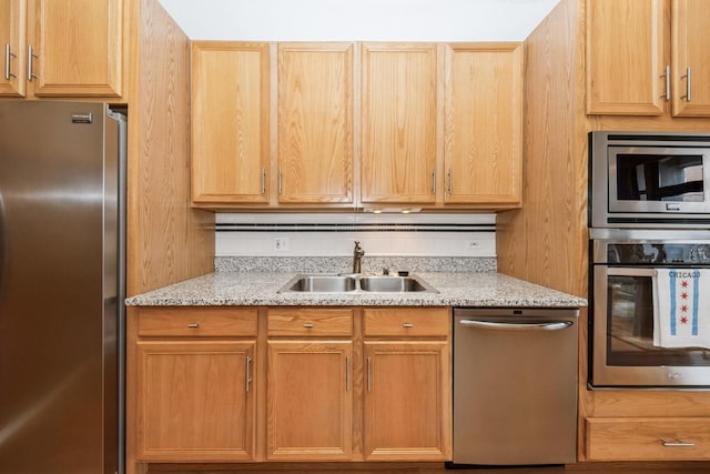 kitchen featuring appliances with stainless steel finishes, sink, light brown cabinetry, and light stone counters