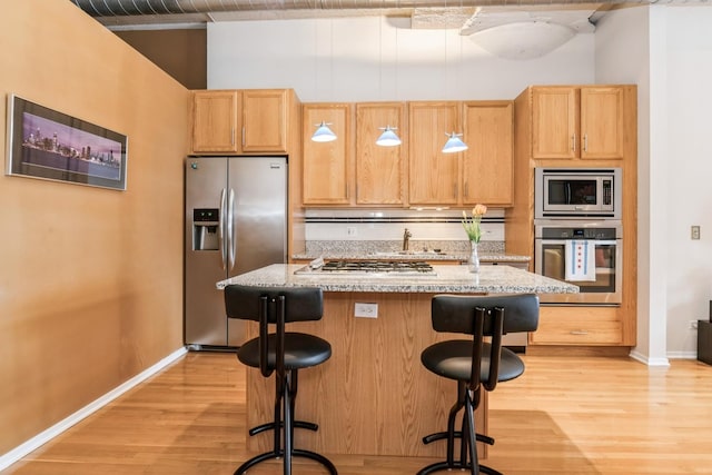 kitchen with a breakfast bar area, light hardwood / wood-style flooring, appliances with stainless steel finishes, an island with sink, and light stone countertops