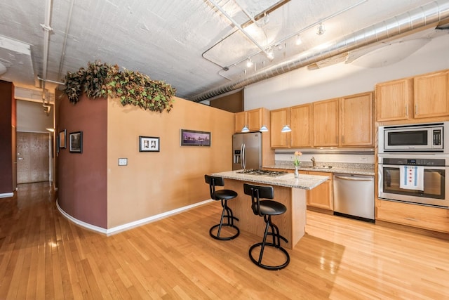 kitchen featuring sink, a breakfast bar area, a kitchen island, stainless steel appliances, and light stone countertops