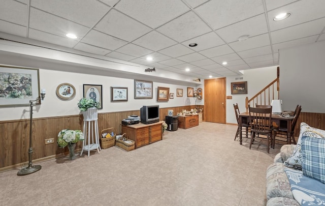 living room featuring a paneled ceiling and wooden walls