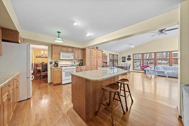 kitchen featuring white appliances, a kitchen breakfast bar, a center island, light stone counters, and light hardwood / wood-style floors