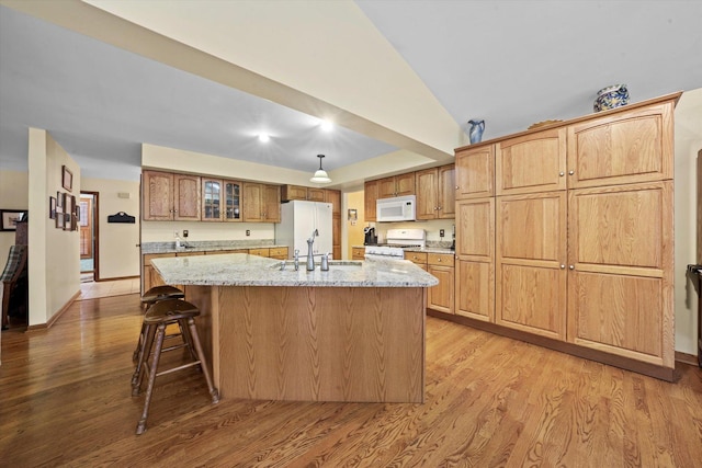 kitchen featuring an island with sink, light wood-type flooring, light stone counters, and white appliances