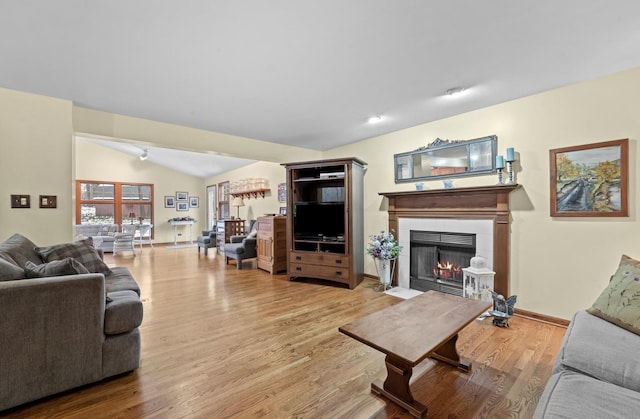 living room featuring a tiled fireplace, vaulted ceiling, and light wood-type flooring