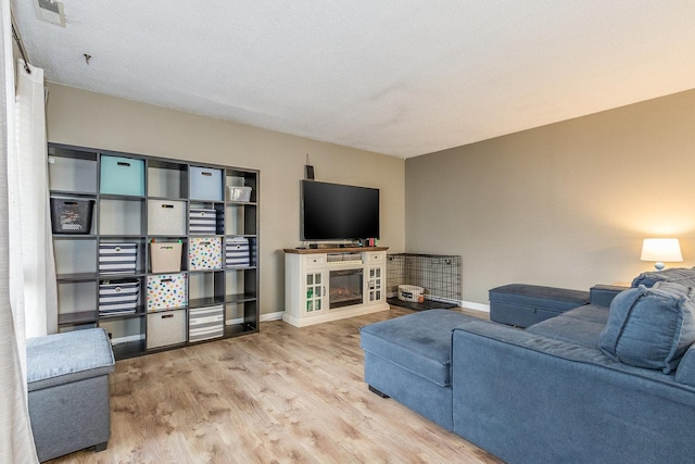 living room featuring visible vents, a glass covered fireplace, a textured ceiling, wood finished floors, and baseboards