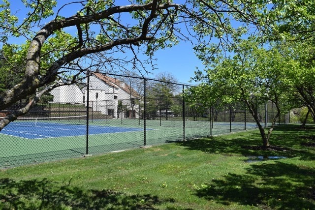 view of tennis court with a yard and fence