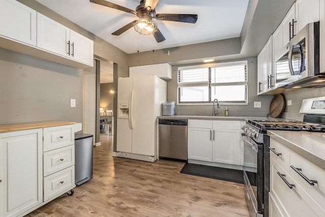 kitchen featuring appliances with stainless steel finishes, white cabinets, a sink, and light wood finished floors