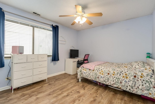 bedroom with light wood-style floors, baseboards, radiator heating unit, and a ceiling fan