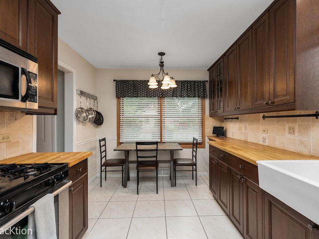 kitchen featuring dark brown cabinetry, stainless steel appliances, decorative light fixtures, and butcher block countertops