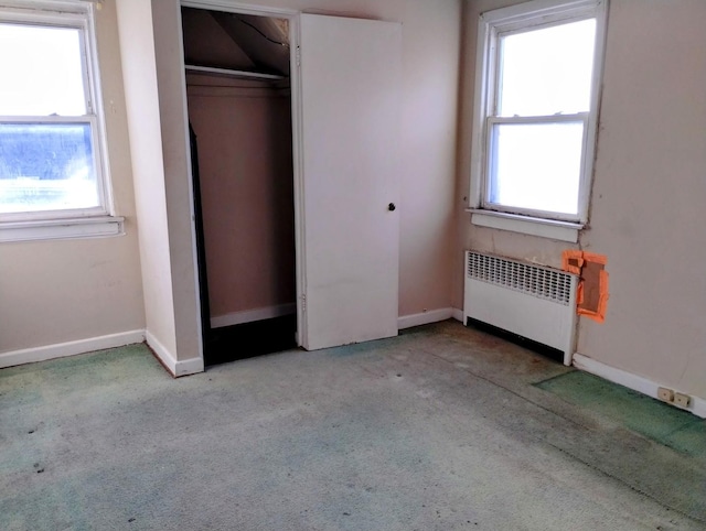 unfurnished bedroom featuring multiple windows, light carpet, radiator heating unit, and a closet