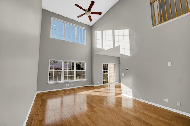 unfurnished living room with wood-type flooring, a towering ceiling, and ceiling fan