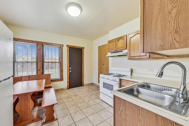 kitchen featuring light tile patterned floors, under cabinet range hood, white appliances, a sink, and light countertops