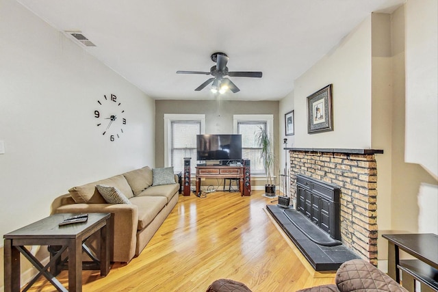 living room with light wood-type flooring, a brick fireplace, ceiling fan, and visible vents