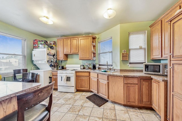 kitchen with light tile patterned floors, a sink, stacked washer / drying machine, white gas range oven, and stainless steel microwave