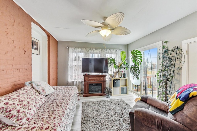 living area featuring ceiling fan, brick wall, and a fireplace