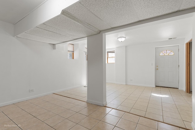 below grade area with light tile patterned floors, a drop ceiling, visible vents, and baseboards