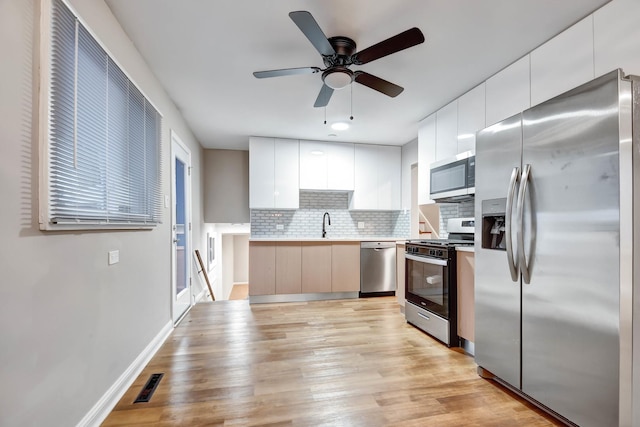 kitchen with light wood-type flooring, white cabinets, ceiling fan, stainless steel appliances, and backsplash