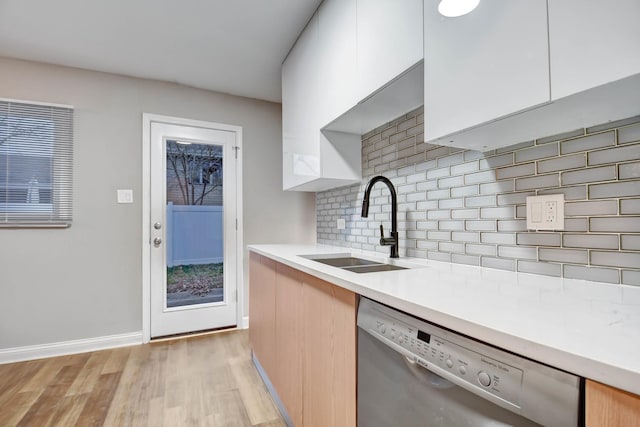 kitchen featuring white cabinetry, sink, backsplash, stainless steel dishwasher, and light hardwood / wood-style floors