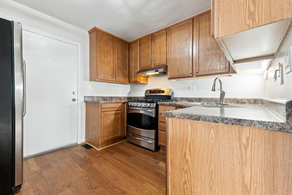 kitchen with appliances with stainless steel finishes, sink, dark hardwood / wood-style flooring, dark stone counters, and kitchen peninsula