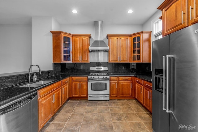 kitchen with wall chimney range hood, sink, dark stone countertops, stainless steel appliances, and decorative backsplash