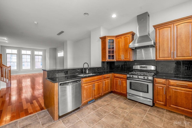 kitchen featuring wall chimney range hood, sink, appliances with stainless steel finishes, dark stone countertops, and decorative backsplash