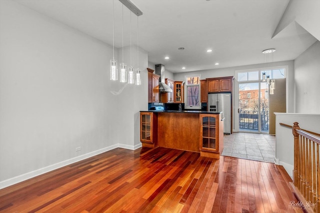 kitchen with pendant lighting, wall chimney range hood, high end fridge, light hardwood / wood-style floors, and kitchen peninsula