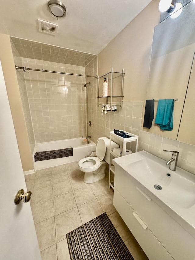 full bathroom with tile walls, tiled shower / bath combo, vanity, toilet, and tile patterned floors