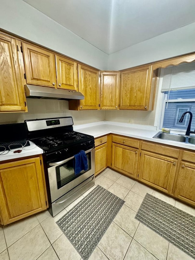 kitchen featuring tasteful backsplash, stainless steel gas range oven, sink, and light tile patterned flooring