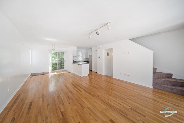 unfurnished living room featuring rail lighting and light hardwood / wood-style floors