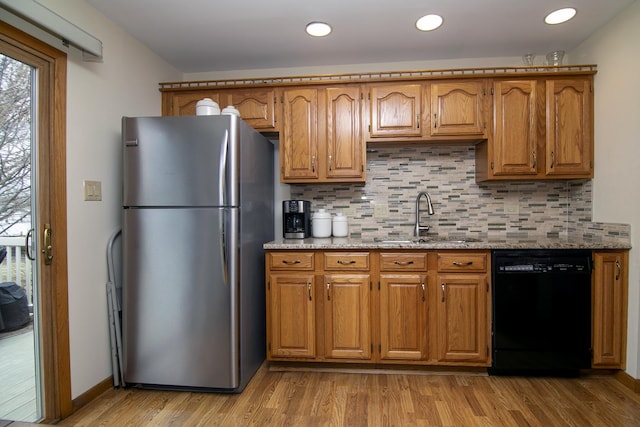 kitchen featuring sink, light hardwood / wood-style flooring, stainless steel refrigerator, black dishwasher, and light stone counters