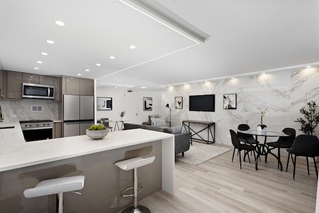 kitchen with appliances with stainless steel finishes, light hardwood / wood-style flooring, a kitchen bar, and kitchen peninsula