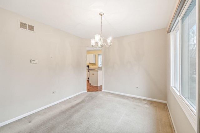 spare room with plenty of natural light, light colored carpet, and a notable chandelier